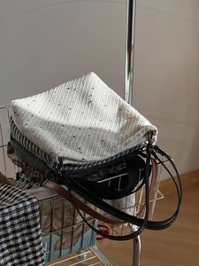 Close-up of multicolored tweed tote bags stacked inside a minimalist silver metal cart