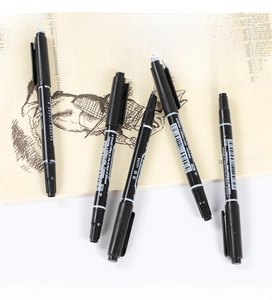 Five double-headed black markers with smooth writing tips displayed on an open book