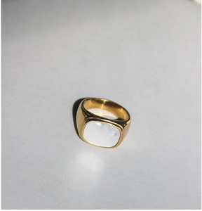 Primer plano detallado de un anillo ancho dorado con incrustación rectangular de concha blanca
