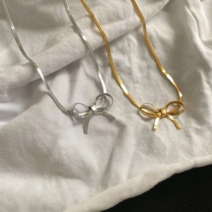 Eleganti collane con ciondolo a fiocco in oro e argento su tessuto bianco liscio