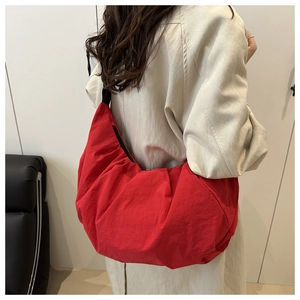 Detail of red oversized nylon shoulder bag with unique pleated texture and black strap