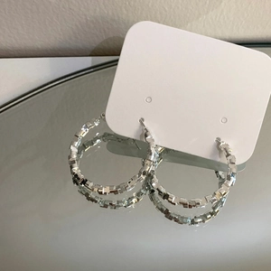 Detailed view of silver hoop earrings with geometric textured facets on a jewelry card