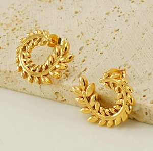 Detailed view of gold wheat-shaped stud earrings on a textured travertine stone base