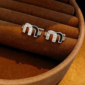 Macro shot of silver letter M earrings with zircon stones and black enamel inlay
