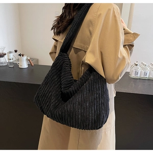 Side view of large black corduroy hobo bag on model in a cozy minimalist cafe setting