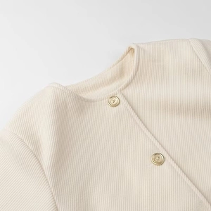 Dettaglio dell'elegante giacca beige strutturata con scollo tondo e bottoni d'oro