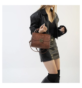 Detail of vintage brown square bag with floral embossing and bronze clasp worn by model