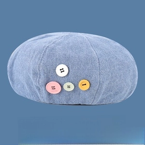 Close-up of light blue denim beret hat featuring four colorful decorative buttons