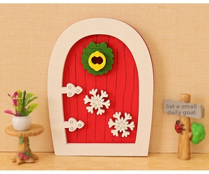 Detailed close-up of a miniature red fairy door with Christmas wreath and snowflakes