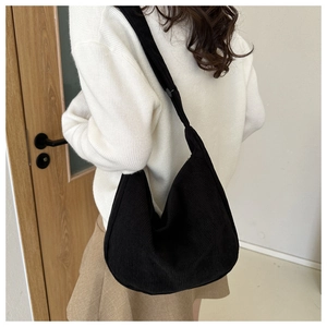 Close-up of black corduroy hobo bag texture with adjustable strap on white sweater