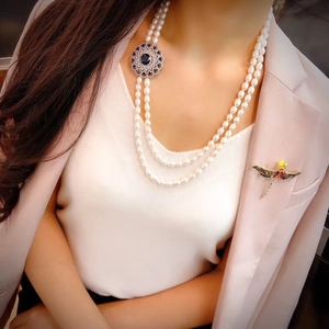 Double-layered white pearl necklace with dragonfly brooch on an elegant suit blazer