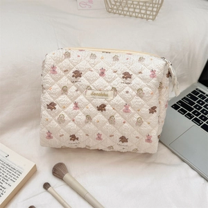 Quilted cream cosmetic bag with cute bear pattern on desk with laptop and brushes