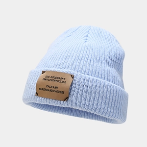 Detail of light blue ribbed beanie featuring a rectangular brown leather decorative patch