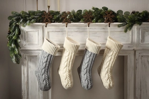 Set of 4 large grey and beige knitted Christmas stockings hanging by a cozy fireplace