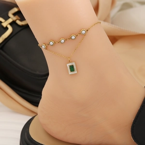 Close-up of double-layer gold anklet with white pearls and a green gemstone charm on ankle