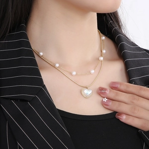Detail of a layered gold snake chain necklace with pearl accents and a heart shell pendant