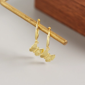 Macro shot of gold butterfly charm earrings with polished finish on a wooden stand