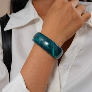 Close-up of a wide translucent dark green acrylic cuff bracelet worn on a white shirt sleeve