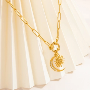 Gold stainless steel necklace with sun and moon pendant on white pleated texture