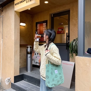 Κοντινή λήψη της ανοιχτόπρασινης κοτλέ τσάντας με σχέδιο smiley σε περιβάλλον καφετέριας