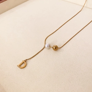 Détail de la chaîne serpent dorée avec une perle et un pendentif en forme de lettre D