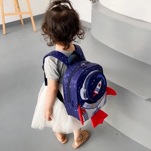 Rear view of a toddler wearing a navy blue rocket backpack with red wings in a daily setting