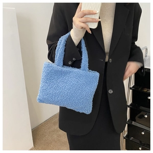 Detail of blue plush teddy handbag held by a model in a minimalist indoor setting