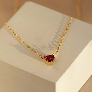 Macro shot of a red heart-shaped gemstone pendant on a gold chain over a jewelry pedestal