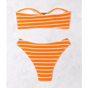 Flat lay of an orange and white striped bikini set on a marble background with textured fabric