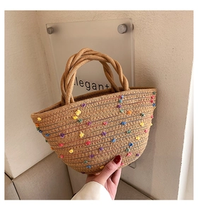 Detail of hand-woven straw bucket bag with colorful pompom embroidery and sturdy handles