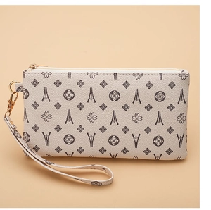 Detail of lychee textured PU leather clutch featuring floral monogram and wrist strap