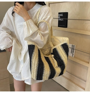Detailed view of woven straw tote bag with black and white stripes and tassel charm