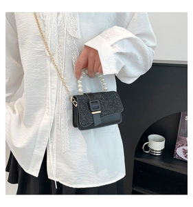 Detail of elegant black mini bag with pearl handle and glitter flap shown on model