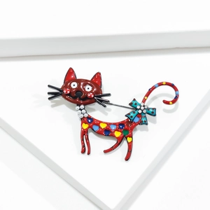 Détail d'une broche chat rouge à pois colorés, collier de perles et nœud bleu brillant