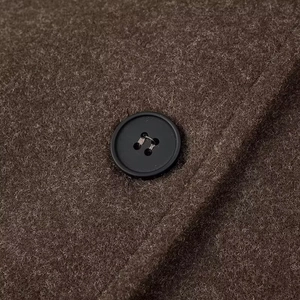 Détail macro de la texture du tissu en laine marron et du bouton noir sur la veste