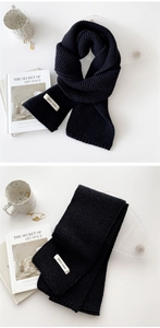 Detail of a thick black knitted scarf with a white brand label on a minimalist background