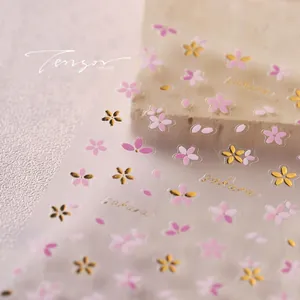 Close-up of pink sakura nail stickers with gold stamping details on textured stone