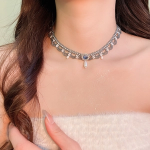 Macro detail of hand-woven beaded lace choker featuring a blue gem and pearl teardrop
