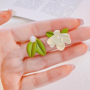 Detail of asymmetric tulip earrings featuring green leaves and white flowers held in hand