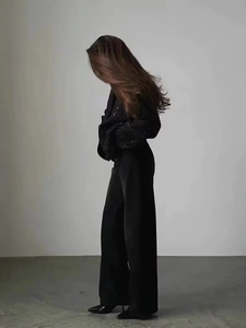 Detail of a black sequined short jacket paired with high-waisted wide-leg trousers