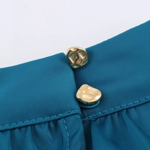Détail d'une robe midi en satin bleu sarcelle avec deux boutons dorés irréguliers