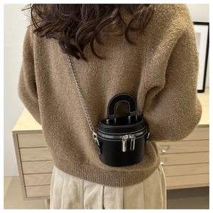 Gros plan d'un sac cylindrique noir élégant avec bandoulière chaîne et zips argentés