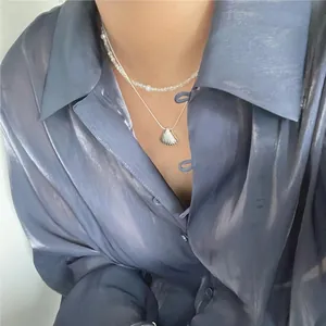 Close-up of layered 925 silver shell pendant and freshwater pearl necklaces on a model