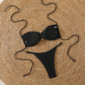 Close-up of black bikini set with gold ring detail on natural woven straw mat background