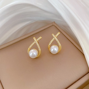 Close-up of gold pearl earrings with crisscross crystal accents on silk fabric