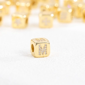 Macro shot of 18k gold plated cube bead with letter M set in sparkling zircon stones