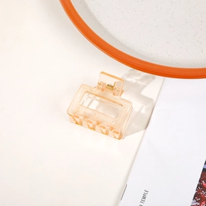 Detail of a transparent orange rectangular hair claw clip with a gold metal spring