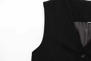 Detail of black asymmetric vest showing woven fabric texture and button closure