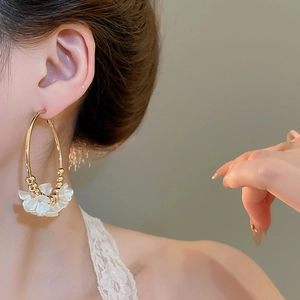 Detail of gold hoop earrings with white acrylic flower charm on a female model