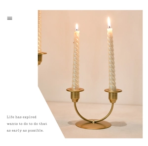Detail of a gold U-shaped metal candle holder with two white spiral candles in a warm setting